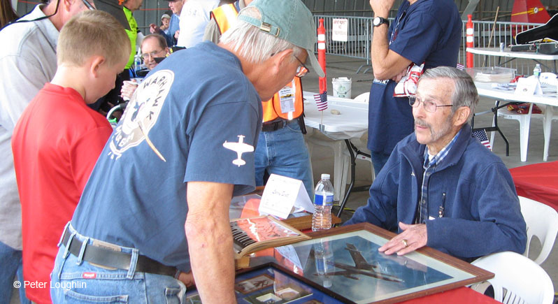 An elderly veteran at a meet-and-greet event showing memorabilia of his military service during the Korean War era.