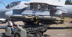 A man on an ordnance loading tractor lifts a cluster of inert bombs onto the underwing pylon of an A-6E Intruder.