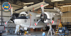 C-1A Trader in a hangar, wings folded, during a maintenance cycle. Photo is from in front and to the left.