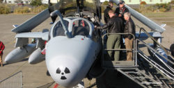 High-angle photo of EA-6B prowler from the front, looking at the plane's nose. The canopies are up, air stairs have been pulled up to the cockpit and civilian spectators are looking into the cockpit.