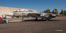 F-14A Tomcat being towed across an airport ramp. It is viewed broadside from the left side. A rounded-roof hangar is in the background.