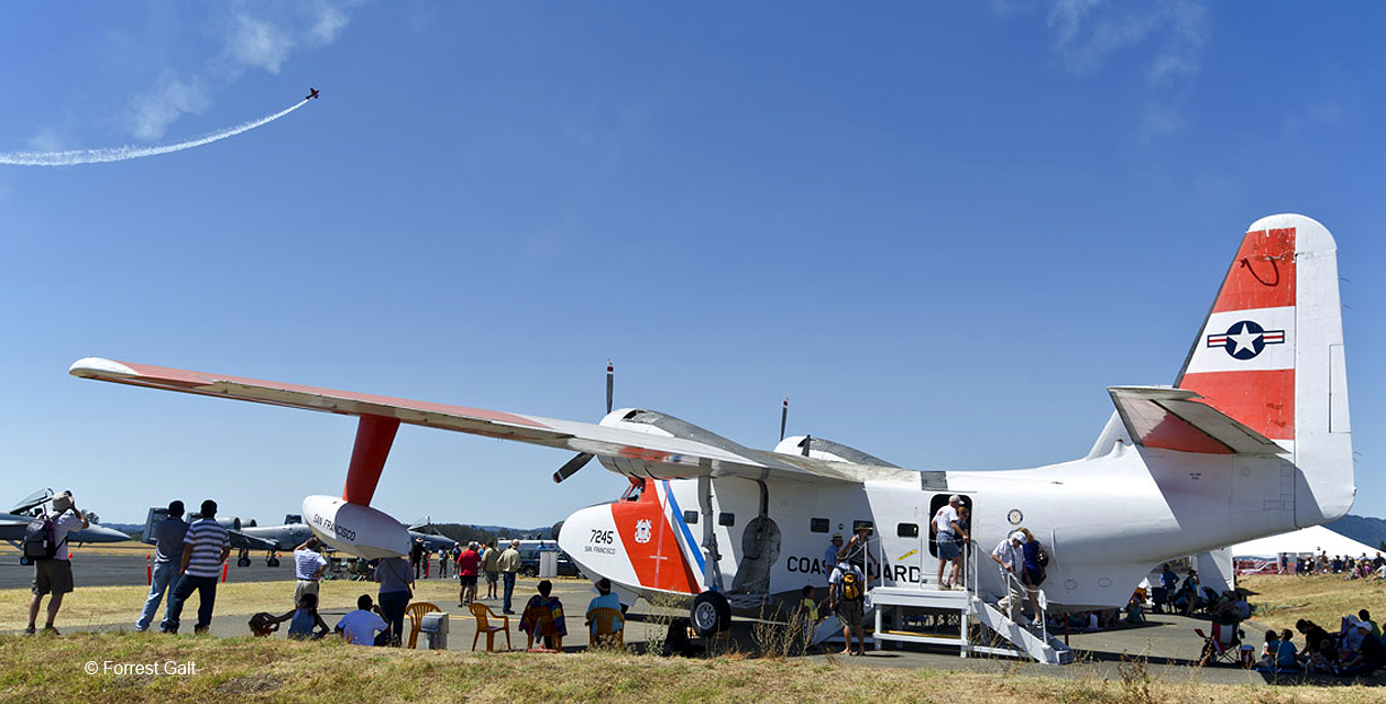 hu16e-albatross-pcam-08 HU-16 Albatross painted in US Coast Guard colors, shown at the Wings Over Wine Country Air Show. People sit in the shade of its large wings, and an aerobatic plane lays a trail of smoke in the background.