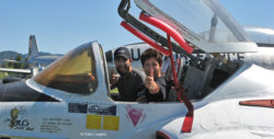 Close-up view from the side of the T-37 Tweet trainer, showing two people sitting in the cockpit giving the thumbs-up.