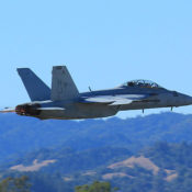 F/A-18 Super Hornet makes a low pass. Hills are in the background. Heat distortion from hot exhaust blurs the background behind the plane's tail pipes.