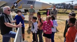 Children on the field at the Pacific Coast Air Museum, with a man explaining something to them.