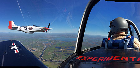 In-flight photograph of a P-51 Mustang, shot from the back seat of a T-28 Trojan trainer. The two are in formation flight with each other.