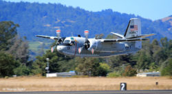 Twin propeller-engined navy C-1A transport flying very low over the runway, with hills in the background
